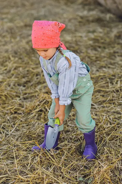 Çiftçi kızın dikey görüntüsü yaz aylarında çiftlikte kürekle saman fırlatıyor. Kırsalda mutlu bir çocukluk. Mutlu yazlar. Kır hayatı, tarım ve kırsal yaşam tarzı.