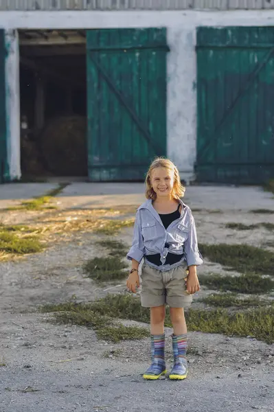 Çiftçi kızın dikey portresi yazın bir çiftlikte eğleniyor. Kırsalda mutlu bir çocukluk. Uzayı metin için kopyala. Mutlu yazlar, açık hava yaşam tarzı