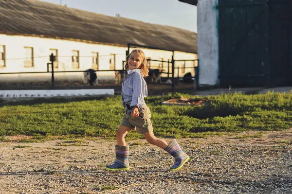 Yazın çiftlikte yürürken gülümseyen çiftçi çocuğun yatay fotoğrafı. Kırsalda mutlu bir çocukluk. Mutlu yazlar, açık hava yaşam tarzı