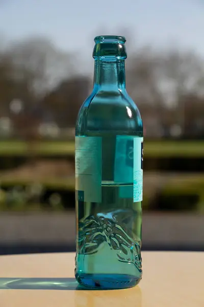 The bottle is half filled with mineral water. A bottle on a table overlooking the park.