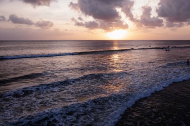 Sörfçüler gün batımında sıcak denizde dalgalara binerler..