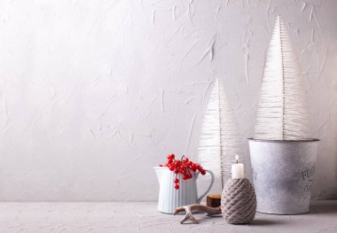 Kış süslemeleri gri, kırmızı ve mavi.. Yanan mum, kış meyveli sürahi, boynuz, gri desenli arka planda beyaz tatil ağaçları. Norven minimalist tarzı. Durgun hayat. 