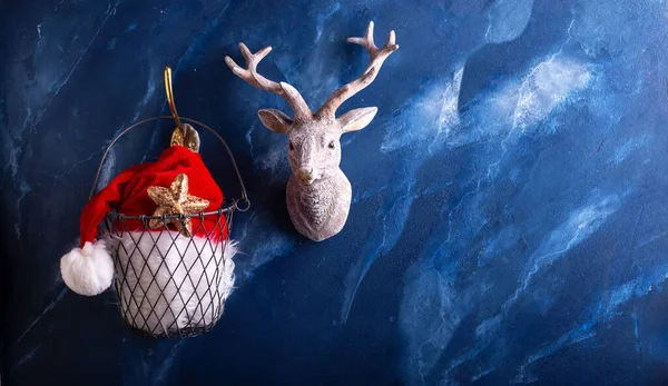 クリスマスのシンボル ワイヤーバスケットにサンタクロースの帽子と濃い青の雑音の背景に鹿 テキスト用の場所 郵便はがき — ストック写真
