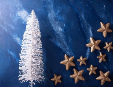 Yeni yıl süslemeleri. Dekoratif beyaz tatil ağacı ve mavi desenli duvarlara karşı altın yıldızlar. Durgun hayat. Noel kutsaması. Metin için yer.
