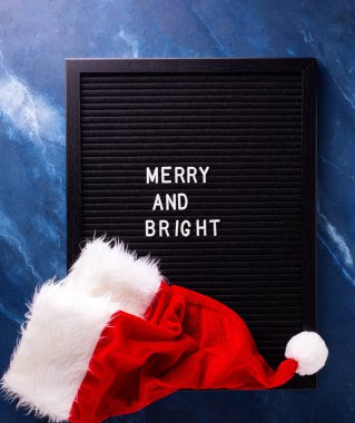 Yılbaşı ya da Noel süslemeleriyle dolu bir arka plan. Siyah tahta, koyu mavi hırıltıda kırmızı Noel Baba şapkası. Durgun hayat. Noel konsepti. Kış tatili kartpostalı.