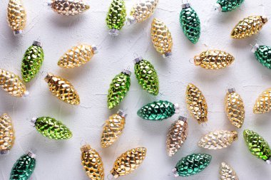 Noel süsleri. Gri desenli arka planda parlak yeşil ve altın renkli dekoratif koniler. Mesaj için yer. Durgun hayat. 