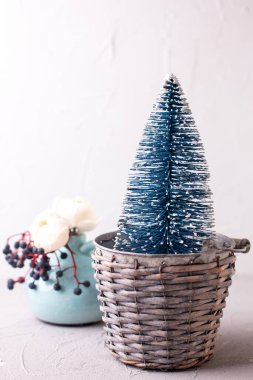 Kartpostalda şenlik süsleri var. Dekoratif mavi bayram ağacı, yabani böğürtlenler ve dokulu duvara karşı vazoda gül çiçekleri. Durgun hayat. Noel konsepti. Boşluğu kopyala.