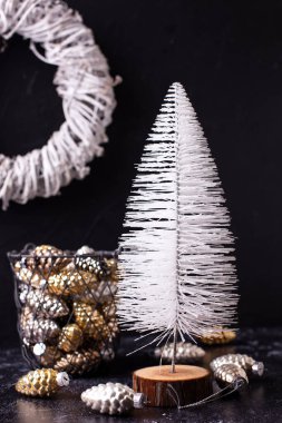 Yeni yıl süslemeleri. Beyaz dekoratif ağaç, kovada parlak koniler ve siyah desenli arka planda beyaz çelenkler. İskandinav minimalist tarzı. Durgun hayat.