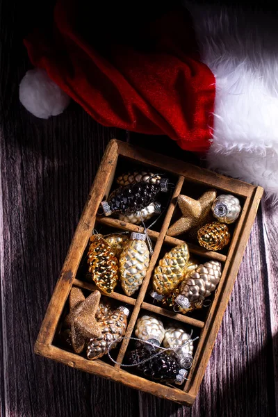 平铺着明亮的圣诞装饰品 老式木箱 玻璃黄金 银质装饰锥和红色圣诞老人帽的老式木制背景 安静的生活 顶部视图 冬季假期明信片 — 图库照片