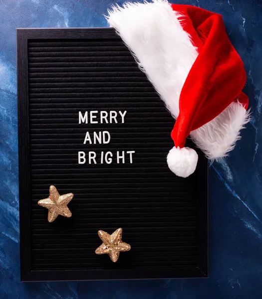 深い青色の雑音に黒のボード サンタクロースと黄金の星の赤い帽子 まだ生きてる クリスマスのコンセプト 冬休みはがき — ストック写真