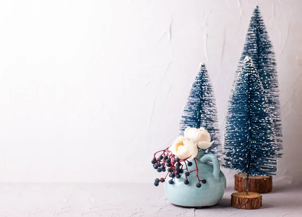 Winter postcard. Decorative  Trees and flowers.  Decorative blue holiday trees and wild berries with rose flowers in vase against textured wall. Still life. Christmas concept.