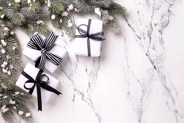 Boxes with wrapped  gifts  in black and white colors  and branches of Christmas tree on white marble background. Top view. Place for text.