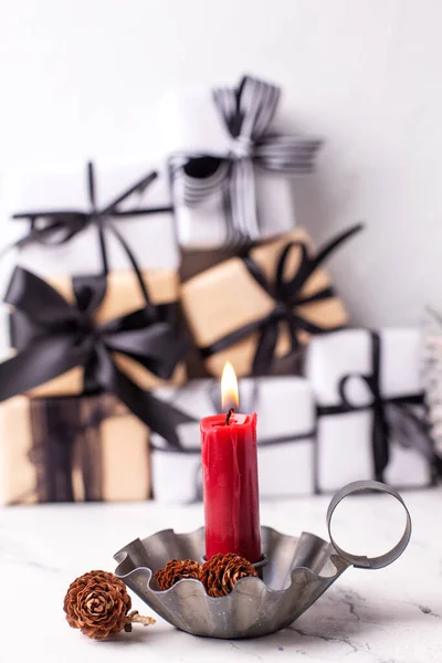 Red burning candle in  vintage candleholder and  boxes with wrapped  gifts  in black and white colors oagainst white textured background. Place for text.