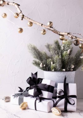 Hediyelerle dolu kutular, kovadaki köknar dalları, beyaz desenli arka planda altın renkli koniler. İskandinav tarzı. Metin için yer.