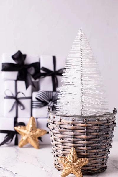 白い質感の背景にプレゼントとラップボックスのグループの前にグレーのバスケットに現代的な白い装飾クリスマスツリー テキストの場所 — ストック写真