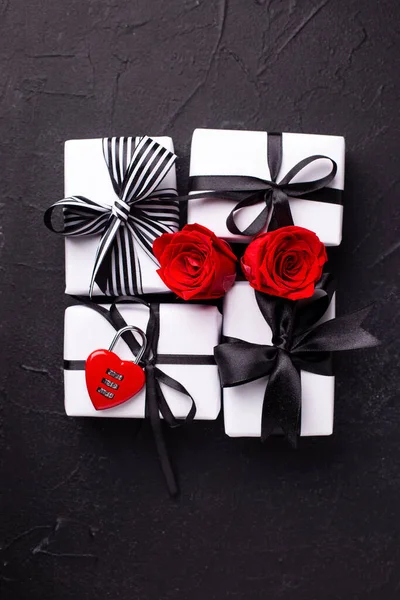 Romantic layout. Wrapped boxes with presents, decorative red lock  and bright red roses flowers on black textured background. Top view. Selective focus is on boxes.