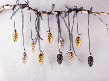 Altın ve siyah koni süslemeleri, ağaç dalında gri desenli duvara asılı siyah kurdeleler üzerinde asılı. Seçici odak.