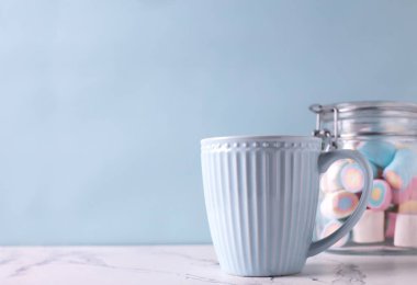 Romantik kartpostal. Mavi bardakta sıcak içecek ve mavi duvarda beyaz mermer arka planda renkli şekerleme kavanozu. Seçici odaklanma. Metin için yer.