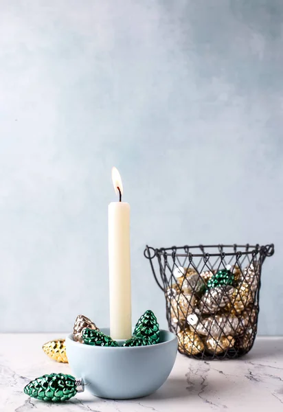 stock image Grenn, golden and silver cones decorations and white burning candle against blue  textured wall. Selective focus is on candle. Place for text.