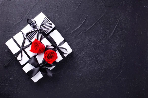 Romantic postcardGroup of wrapped boxes with presents  and bright red roses flowers on black textured background. Place for text. Top view. Selective focus is on boxes.