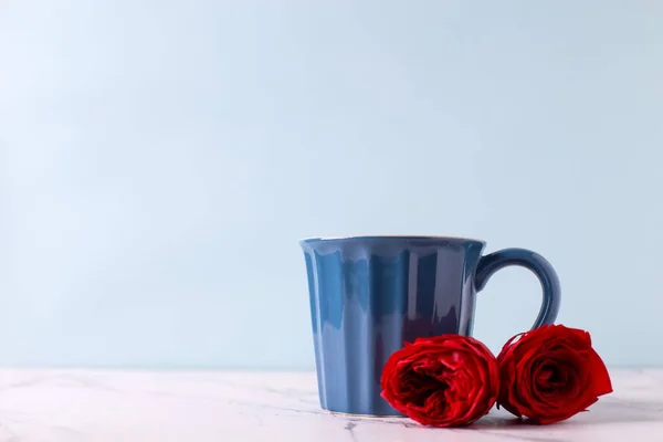 浪漫的情人节明信片 深蓝色杯子 红玫瑰 白色大理石背景 蓝色墙壁衬托 选择性的焦点放在杯子上 案文的位置 — 图库照片