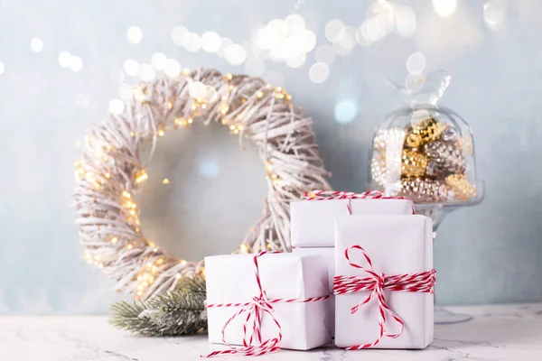 Composition with  wrapped boxes with gifts, wreath with fairy lights, branches of fir tree and golden decoration on white marble against  blue textured  wall. Place for text.