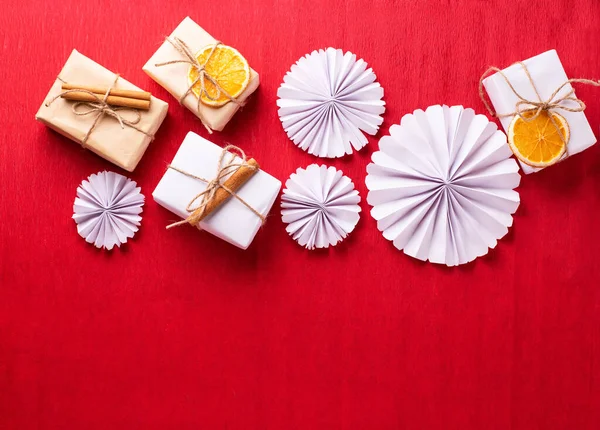 Decorations in scandinavian style. Wrapped boxes decorated cinnamon and dried oranges, paper rosettes on red paper textured background. Top view. Place for text.