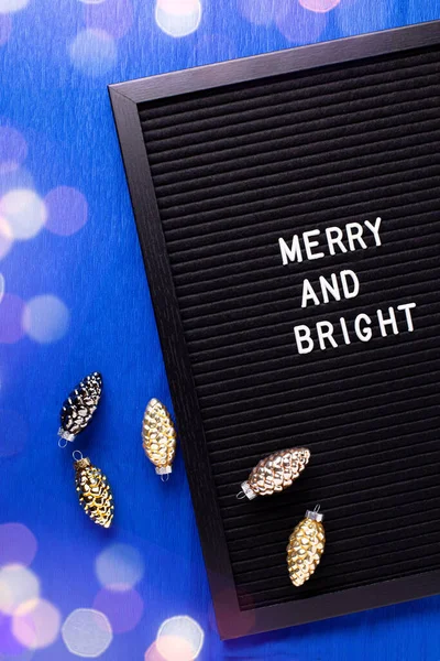 圣诞明信片 写字板上写着快乐而明亮的金色圆锥装饰哦 明亮的蓝纸质感的背景 顶部视图 Bokeh灯 — 图库照片