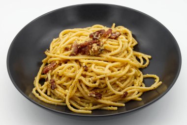 İtalyan spagettisi alla Carbonara Makarnası, beyaz üzerine izole edilmiş siyah bir tabakta..