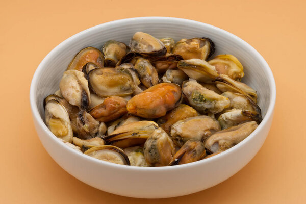 Peeled mussels in a bowl on orange background.