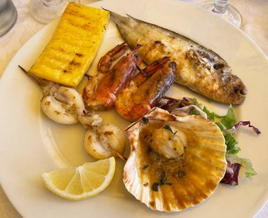 Masadaki beyaz tabakta ızgara deniz ürünleri. 