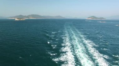 Denizdeki adaların yanından geçerken beyaz su izi bırakan bir feribot. Göktaşı manzaralı. 4K