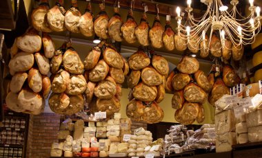 Bologna - İtalya - 27 Aralık 2024: Bir İtalyan şarküterisinin iyileşmiş prosciutto 'sunun çeşitli peynir çeşitleriyle birlikte sergilenmesi.
