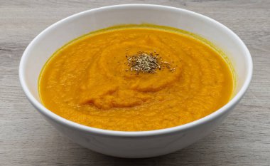 Lezzetli portakallı kremalı çorba, muhtemelen balkabağı veya tereyağlı kabaktan yapılır, aromatik kurutulmuş otlarla güzelce süslenir ve hafif ahşap bir yüzey üzerinde sunulur..