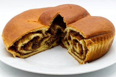 Lezzetli yuvarlak tatlı bir ekmek, muhtemelen fındık rulosu ya da tatil pastası, zengin bir spiral ile beyaz bir tabakta kesilmiş..