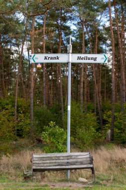 Sick and healing - signpost behind an old bench - German text clipart