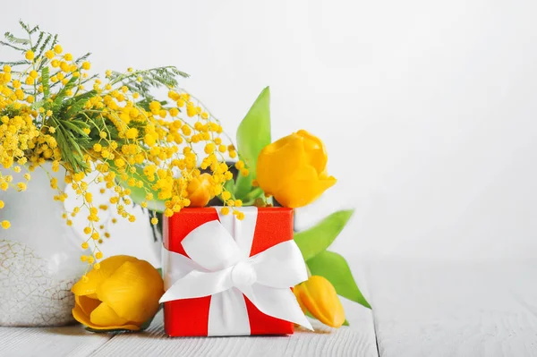 Happy Women\'s Day, Valentine\'s Day concept. Happy March 8 greeting card. Giftbox with Mimosa fresh flowers and yellow tulips on light background with empty space