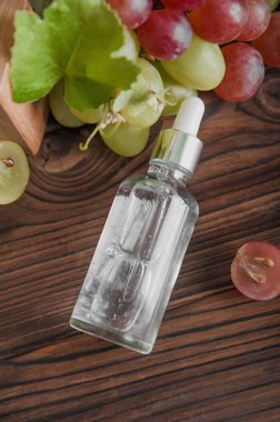Ahşap trend podyumda serum ve kesilmiş üzümler. Cilt bakımı, üzüm tohumu yağının sağlık konsepti. Üst görünüm