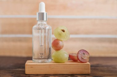 Ahşap trend podyumda serum ve kesilmiş üzümler. Cilt bakımı, üzüm tohumu yağının sağlık konsepti. Üst görünüm