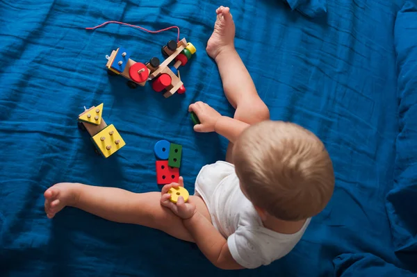Toddler boy plays with wooden constructor train on bed close-up..