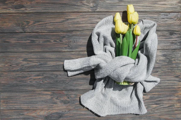 Gray sweater and yellow tulips on textured wooden background