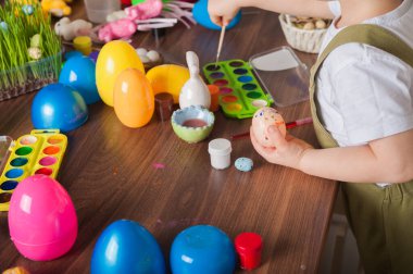 Toddler boy painting Easter egg close-up. Easter traditions and entertainment with children at home.