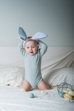 Bebek 1 yaşında yatakta sepeti ve paskalya yumurtaları var. Yumurta avı, çocuk aktivitesi.