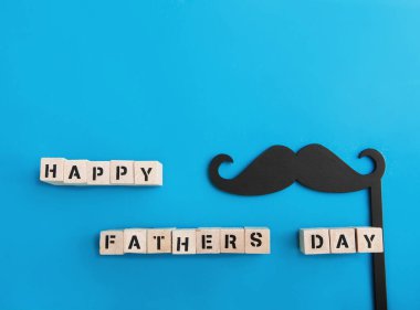 Inscription Happy Fathers Day and black mustache decor on blue background.