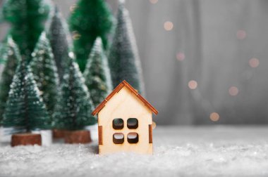 Mutlu Noeller ve mutlu yıllar tebrik kartı. Noel ağaçlarının arka planında minyatür ev modeli.