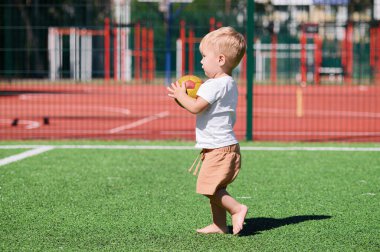 2 yaşında bir çocuk futbol sahasında topla oynuyor..