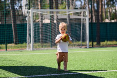 2 yaşında bir çocuk futbol sahasında topla oynuyor..