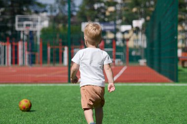 2 yaşında bir çocuk futbol sahasında topla oynuyor..