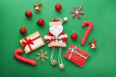 Noel ruhu ve neşeli bir tatil dekorasyonu. Parlak yeşil bir arkaplanda, büyüleyici bir Noel Baba figürü, parlak kırmızı süsler, altın çanlar var.