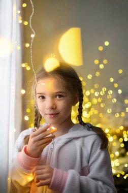 Arka planda Neşeli Çiçek Işıklarıyla Pencereden Dışarı Bakan Kız.